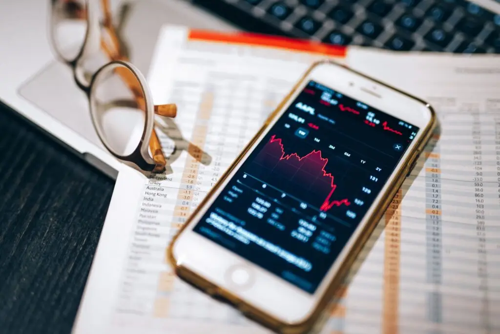 Adani Power Share Price Today 3 Smartphone displaying stock market chart on a financial spreadsheet with eyeglasses.