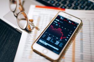 Adani Power Share Price Today 3 Smartphone displaying stock market chart on a financial spreadsheet with eyeglasses.